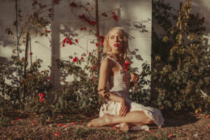 Editorial lifestyle fashion portrait in rose bushes bare feet and classic red lip makeup and blonde wavy hair